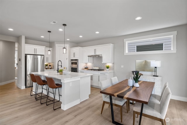 kitchen with decorative light fixtures, an island with sink, white cabinets, stainless steel appliances, and light stone countertops