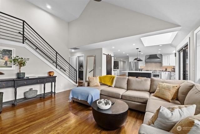 living room with hardwood / wood-style floors, a towering ceiling, a skylight, and a barn door