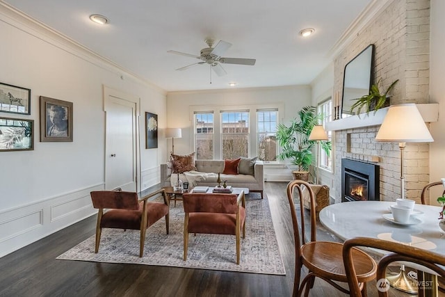 living area featuring a wainscoted wall, dark wood-type flooring, a brick fireplace, and crown molding