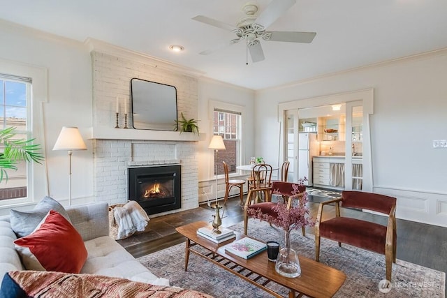 living room featuring a wainscoted wall, dark wood-type flooring, a fireplace, and crown molding