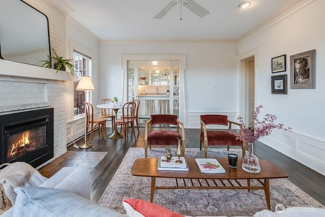 living area with dark wood-style floors, wainscoting, a fireplace, and crown molding