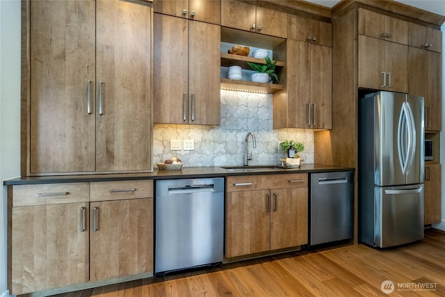 kitchen with light wood-style flooring, a sink, appliances with stainless steel finishes, open shelves, and dark countertops