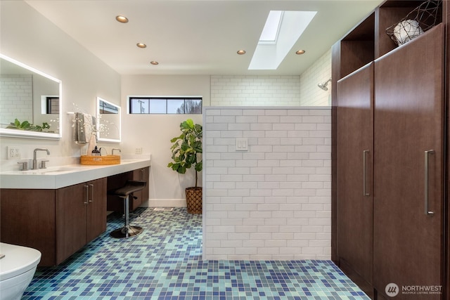 full bath with double vanity, a skylight, toilet, a walk in shower, and a sink