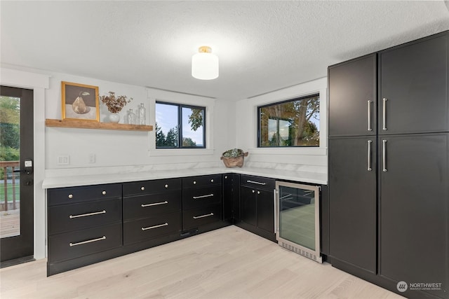 kitchen with a textured ceiling, beverage cooler, and light wood-type flooring