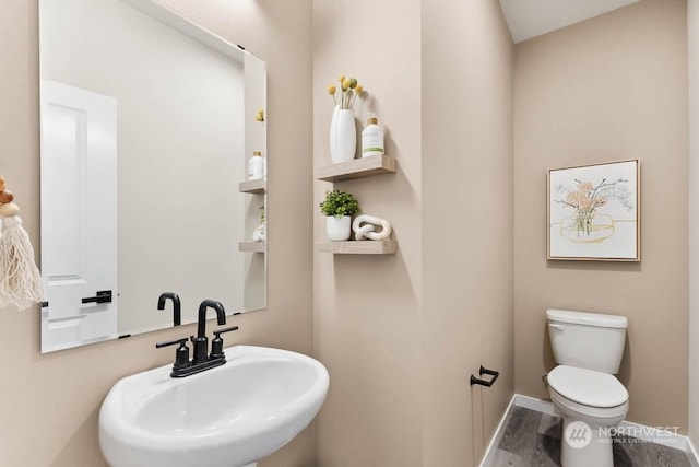 half bathroom featuring toilet, baseboards, a sink, and wood finished floors