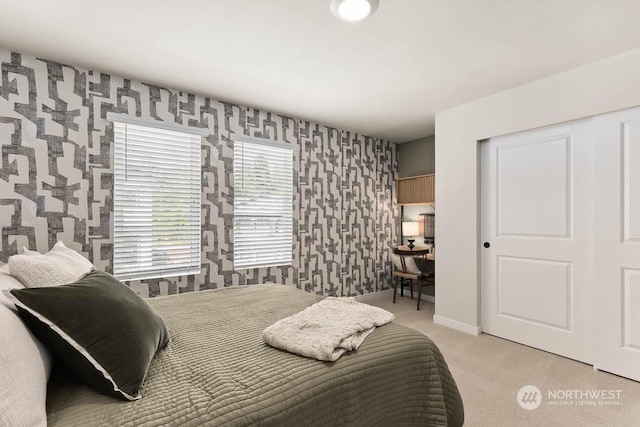 bedroom featuring a closet, light colored carpet, baseboards, and wallpapered walls