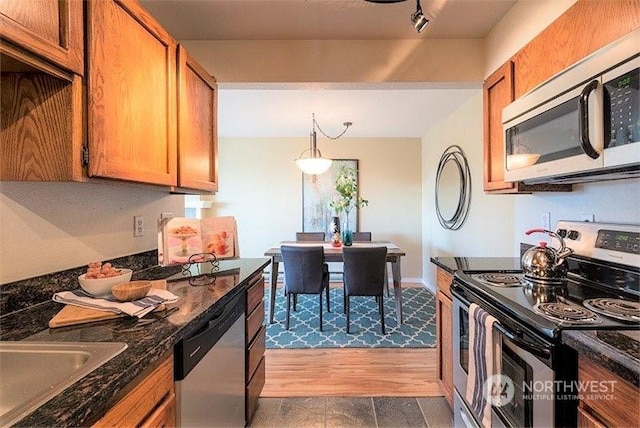 kitchen with sink, dark stone countertops, track lighting, appliances with stainless steel finishes, and pendant lighting