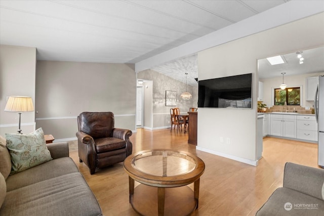 living room with lofted ceiling with beams, sink, and light hardwood / wood-style flooring