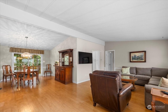 living room featuring vaulted ceiling with beams, a notable chandelier, and light hardwood / wood-style floors