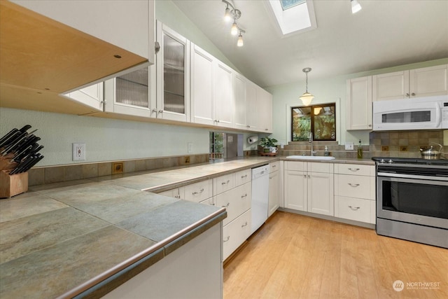 kitchen with vaulted ceiling with skylight, sink, white cabinets, hanging light fixtures, and white appliances