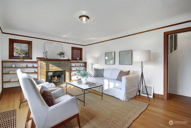 living room with crown molding, a tile fireplace, and light hardwood / wood-style flooring