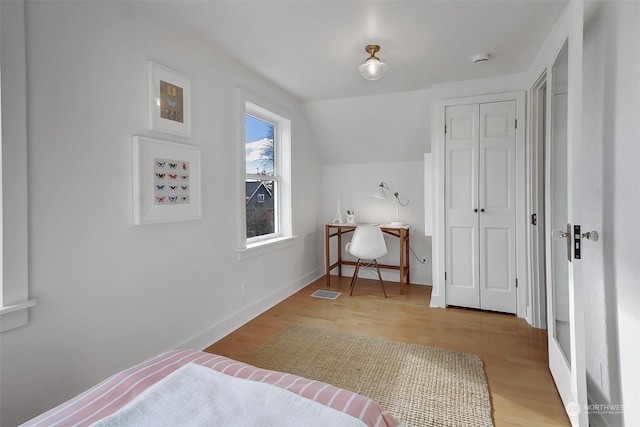 bedroom featuring wood-type flooring, vaulted ceiling, and a closet