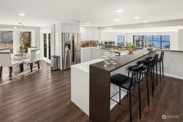 kitchen featuring dark wood-style floors, a breakfast bar area, white cabinetry, stainless steel fridge, and a peninsula