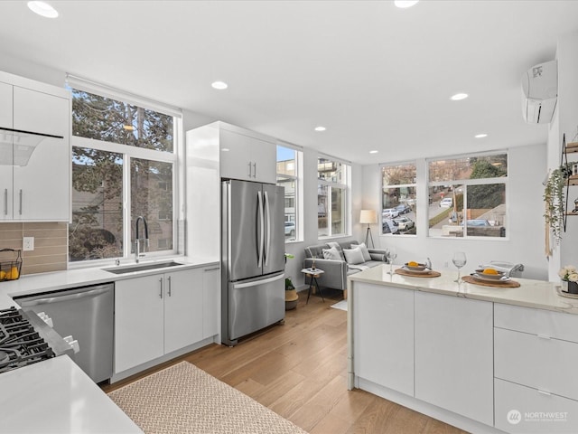 kitchen with appliances with stainless steel finishes, white cabinetry, sink, backsplash, and light hardwood / wood-style flooring