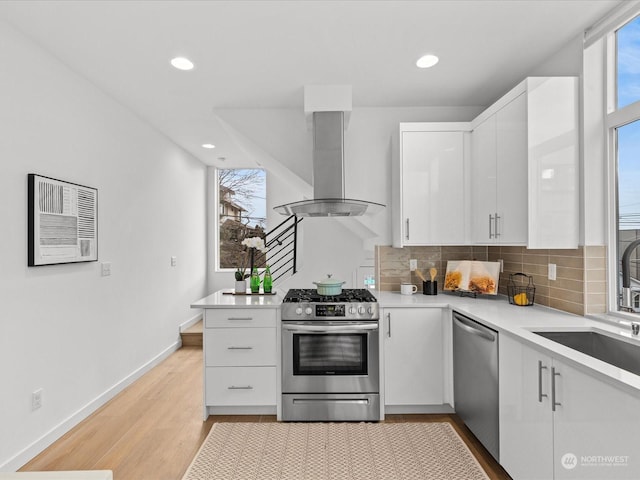 kitchen featuring sink, island range hood, appliances with stainless steel finishes, decorative backsplash, and white cabinets