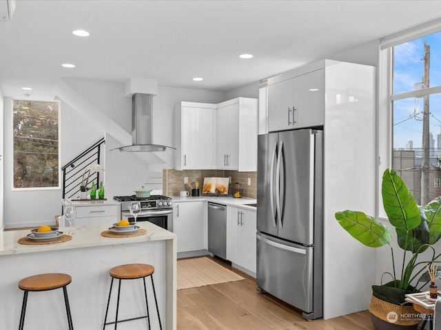 kitchen featuring extractor fan, a breakfast bar, white cabinetry, stainless steel appliances, and light hardwood / wood-style flooring