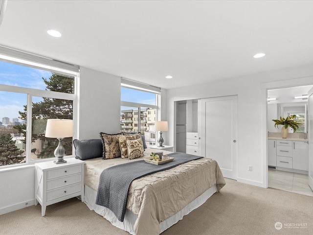 bedroom with ensuite bath, light colored carpet, and a closet