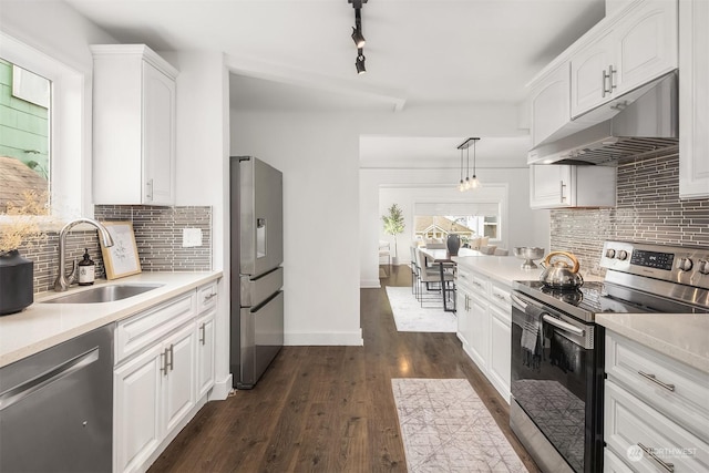 kitchen featuring under cabinet range hood, stainless steel appliances, a sink, hanging light fixtures, and light countertops