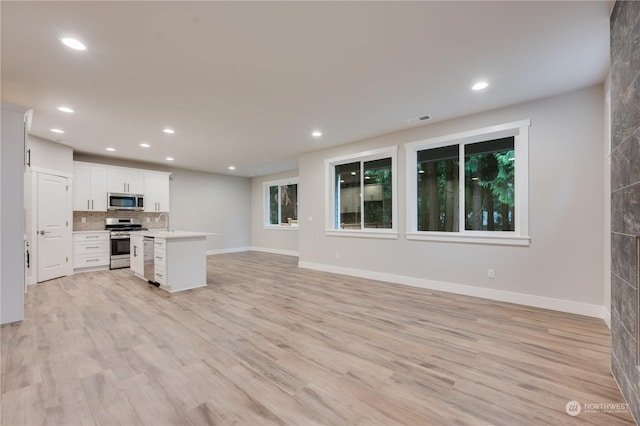 kitchen with appliances with stainless steel finishes, white cabinets, a kitchen island, decorative backsplash, and light wood-type flooring