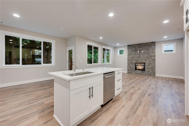 kitchen with sink, a kitchen island with sink, a large fireplace, white cabinets, and stainless steel dishwasher