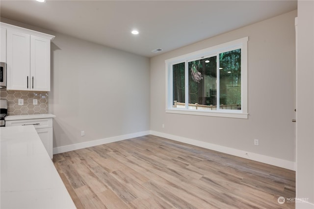 kitchen featuring decorative backsplash, light hardwood / wood-style flooring, and white cabinets