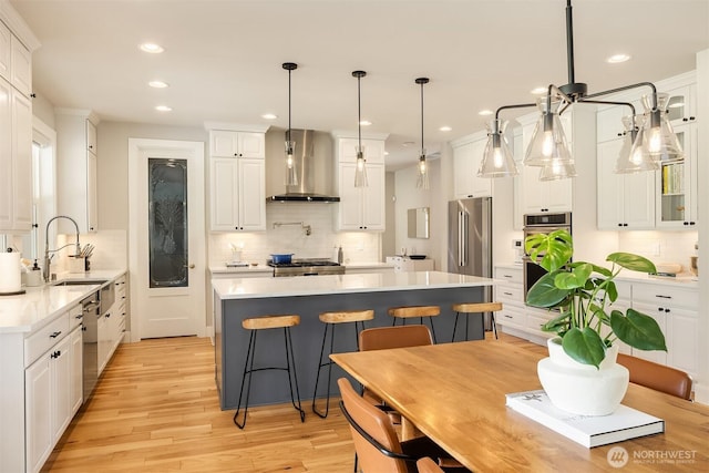 kitchen with white cabinetry, light countertops, wall chimney range hood, appliances with stainless steel finishes, and light wood-type flooring