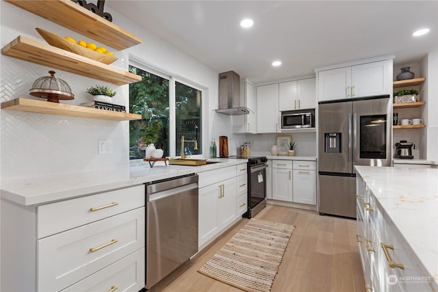 kitchen with white cabinets, wall chimney exhaust hood, stainless steel appliances, light stone countertops, and light hardwood / wood-style flooring