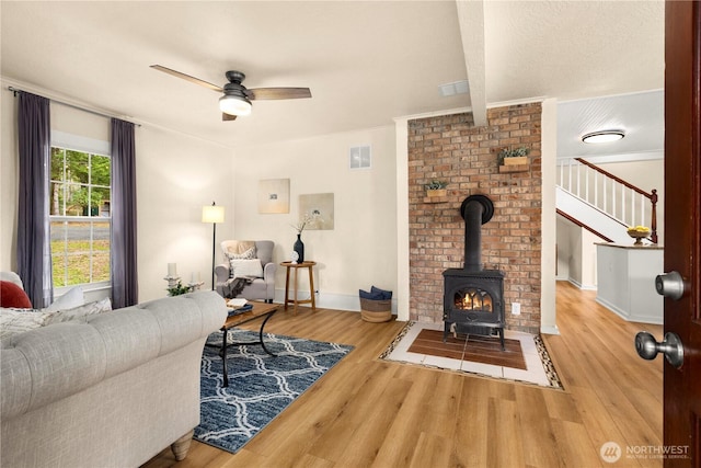 living area featuring visible vents, baseboards, ceiling fan, a wood stove, and wood finished floors