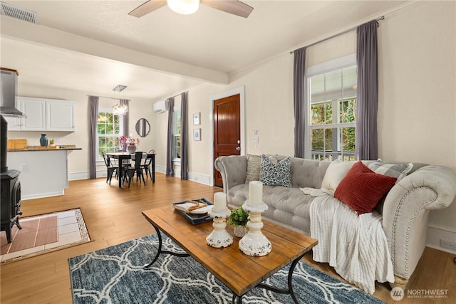 living room featuring a ceiling fan, visible vents, light wood finished floors, baseboards, and a wall mounted air conditioner