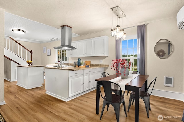 kitchen featuring a peninsula, ornamental molding, white cabinets, light wood-style floors, and island range hood