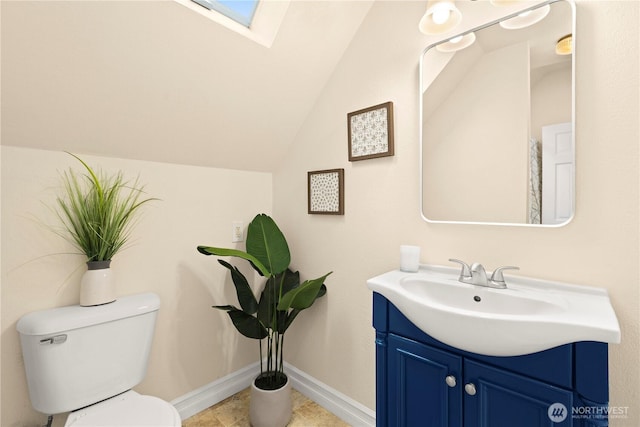 bathroom featuring vanity, vaulted ceiling with skylight, toilet, and baseboards