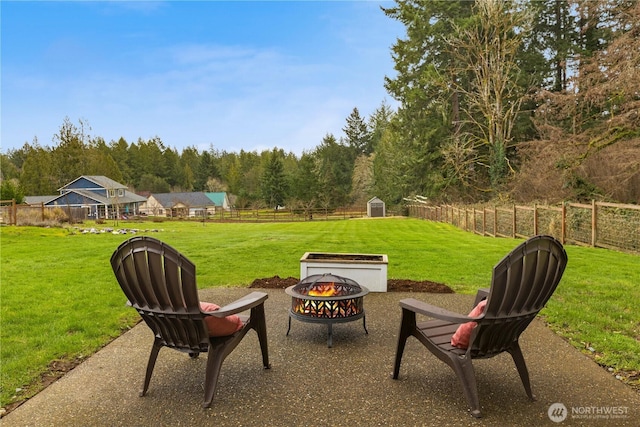 view of patio featuring an outbuilding, a shed, fence, a forest view, and a fire pit