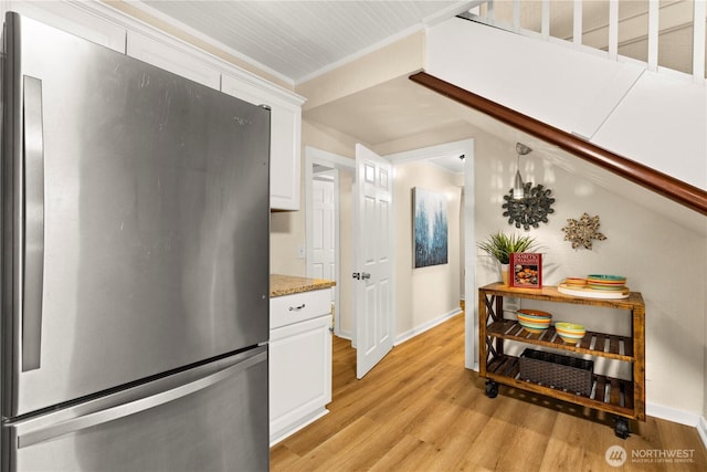 kitchen with crown molding, light wood-type flooring, light stone counters, freestanding refrigerator, and white cabinets