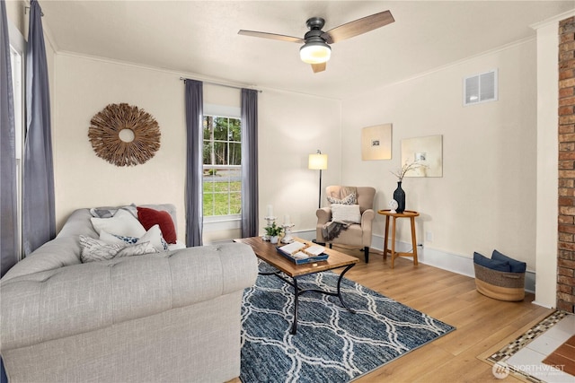 living room with wood finished floors, baseboards, visible vents, ceiling fan, and ornamental molding