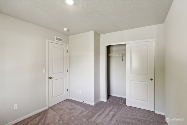 unfurnished bedroom featuring a textured ceiling, dark carpet, and a closet