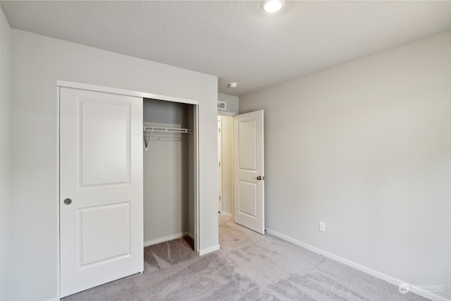 unfurnished bedroom with light carpet, a textured ceiling, and a closet