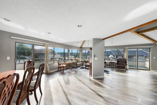 dining space with lofted ceiling with beams, plenty of natural light, a textured ceiling, and light hardwood / wood-style floors