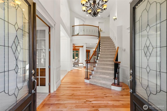 foyer entrance with an inviting chandelier, a towering ceiling, and light hardwood / wood-style flooring