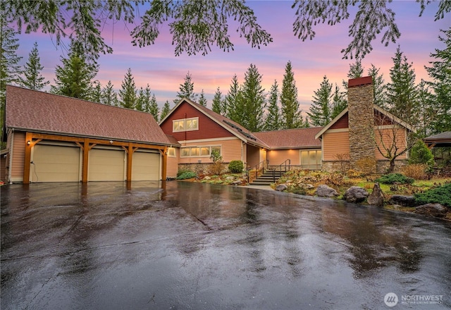 view of front facade featuring a garage, driveway, a shingled roof, and a chimney