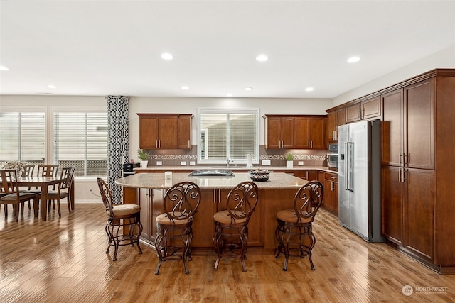 kitchen with stainless steel appliances, light hardwood / wood-style flooring, a kitchen island, light stone counters, and a kitchen bar