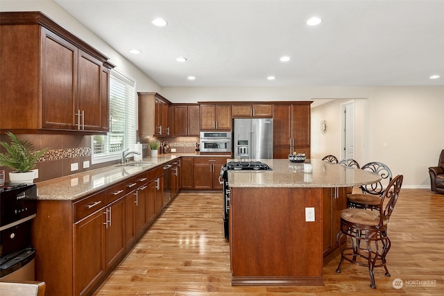 kitchen featuring appliances with stainless steel finishes, a kitchen breakfast bar, a center island, backsplash, and sink