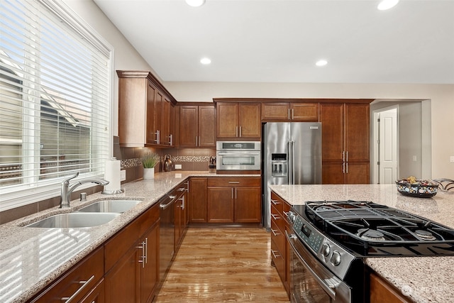 kitchen with appliances with stainless steel finishes, sink, light wood-type flooring, light stone countertops, and tasteful backsplash