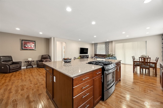 kitchen featuring light wood-type flooring, light stone countertops, a center island, and stainless steel gas range