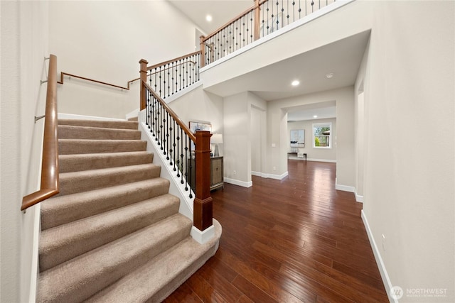 stairway featuring recessed lighting, a towering ceiling, hardwood / wood-style flooring, and baseboards