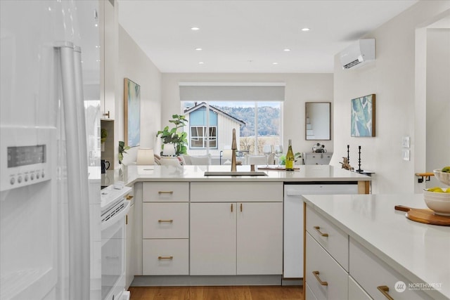 kitchen featuring sink, light wood-type flooring, an AC wall unit, white appliances, and white cabinets