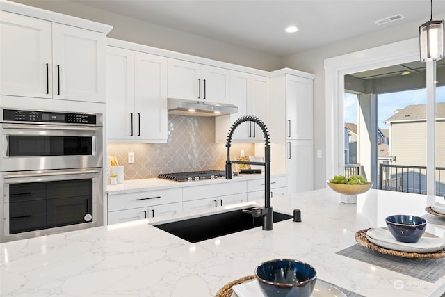 kitchen featuring light stone countertops, appliances with stainless steel finishes, pendant lighting, and white cabinets