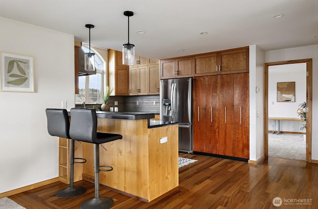 kitchen featuring decorative light fixtures, brown cabinets, stainless steel refrigerator with ice dispenser, dark countertops, and a peninsula