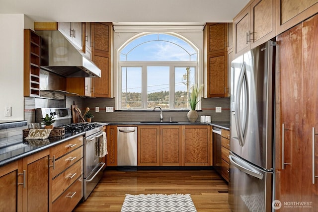 kitchen with under cabinet range hood, stainless steel appliances, a sink, brown cabinets, and dark countertops