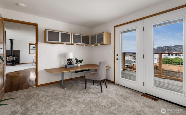 office space featuring a wood stove, baseboards, visible vents, and light colored carpet