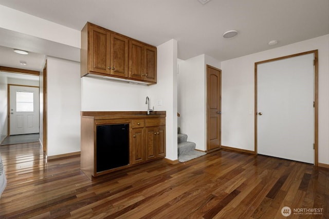 kitchen featuring dark wood-style floors, baseboards, brown cabinetry, and a sink